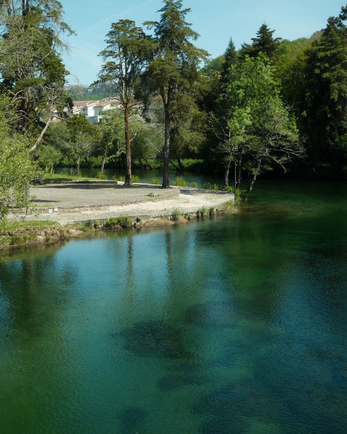 O rio Vez em Arcos de Valdevez, largo e parado, com as árvores da margem refletidas na água e as casas da vila ao fundo.